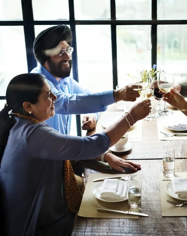 Four colleagues raising their glasses across a set dinner table by a tall window.